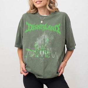Puede incluir: Camiseta verde oliva con un dise&ntilde;o gr&aacute;fico verde de un castillo con fuegos artificiales y la palabra "Disneyland". La camiseta tiene mangas cortas y un corte holgado.