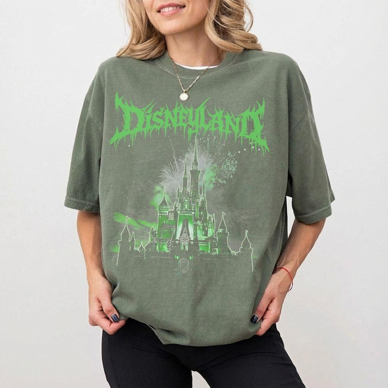 Puede incluir: Camiseta verde oliva con un dise&ntilde;o gr&aacute;fico verde de un castillo con fuegos artificiales y la palabra "Disneyland". La camiseta tiene mangas cortas y un corte holgado.