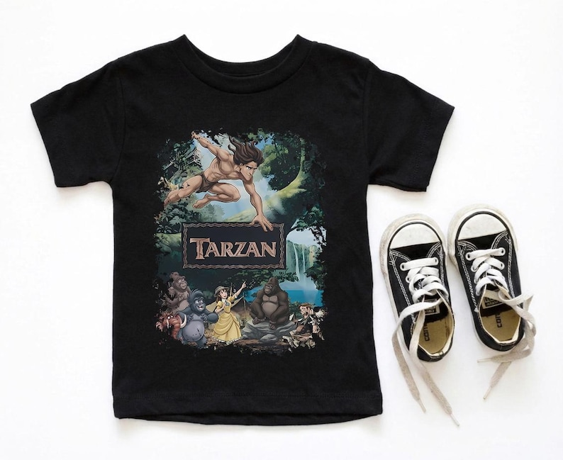 May include: Black t-shirt featuring a colorful graphic of Tarzan, the jungle hero, with the word "Tarzan" in a brown frame. The shirt is paired with black canvas sneakers with white laces.