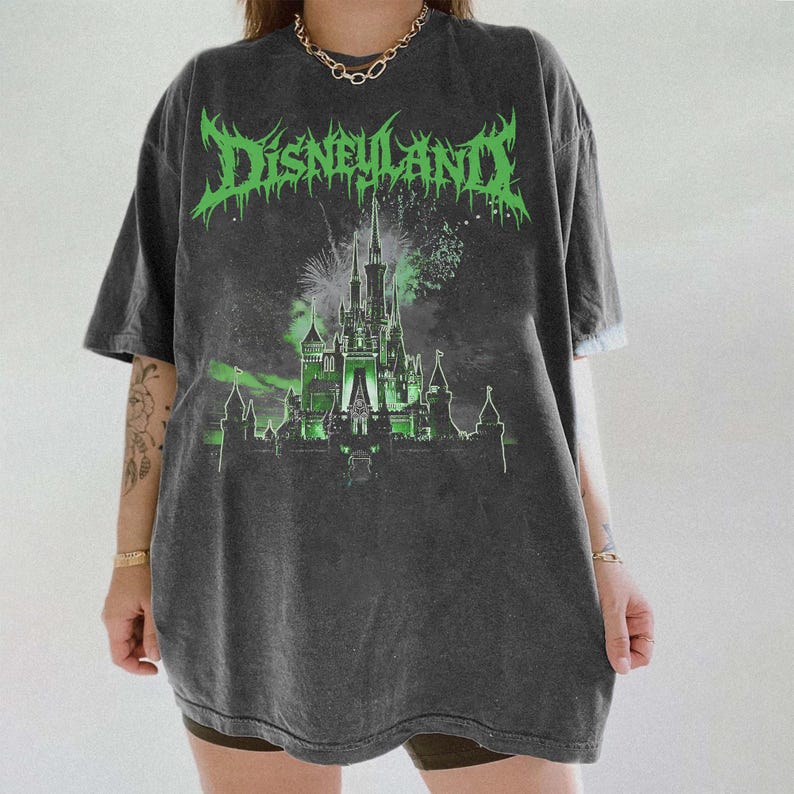 Puede incluir: Camiseta gris oscuro con aspecto desgastado. La parte delantera presenta la palabra "Disneyland" en verde, con letras g&oacute;ticas, sobre una ilustraci&oacute;n de castillo iluminado en verde con fuegos artificiales.