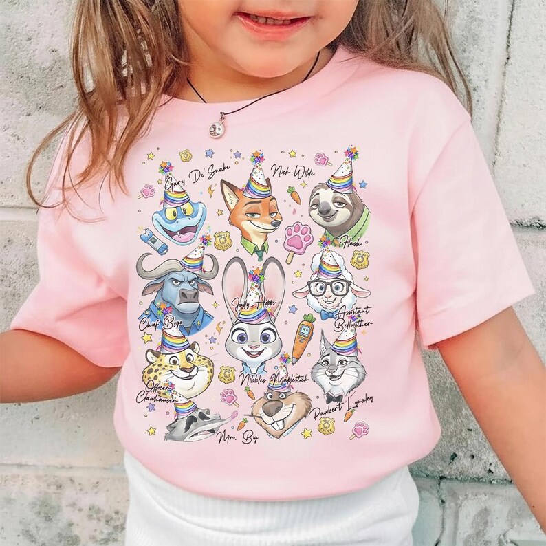 Op de afbeelding: Roze T-shirt met korte mouwen met een kleurrijke afbeelding van cartoon dierenfiguren met feesthoeden. Het ontwerp bevat een vos, konijn, luiaard en anderen, met namen erboven. Versierd met sterren en feestsymbolen.