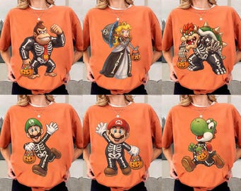 Könnte beinhalten: Eine Kollektion von sechs orangefarbenen T-Shirts, die jeweils eine andere Nintendo-Figur in einem Skelettkostüm für Halloween zeigen. Die Figuren sind Donkey Kong, Prinzessin Peach, Bowser, Luigi, Mario und Yoshi, die alle Kürbiseimer halten.