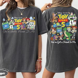 Może przedstawiać: Ciemnoszara koszulka z kolorową grafiką postaci z Toy Story oraz napisem "Toy Story 5" i "You've Got a Friend In Me". Koszulka ma luźny kr&oacute;j i kr&oacute;tkie rękawy.