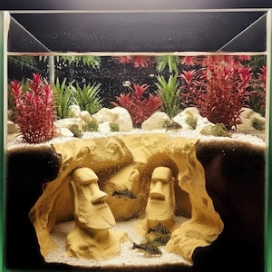 May include: A rectangular aquarium with a unique underwater scene. The tank features two Moai statues, sand, and live plants. The plants are a mix of green and red, creating a vibrant environment for the fish.