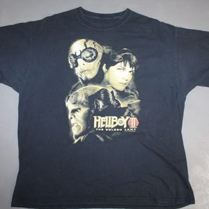 May include: A dark blue t-shirt with a graphic print of the characters from the movie "Hellboy II: The Golden Army".