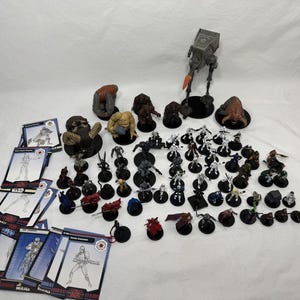 May include: A collection of Star Wars miniature figurines and game cards. The set includes various alien creatures, humanoids, and a grey AT-ST walker with an orange blast effect. The cards feature line art illustrations of characters and Star Wars branding.