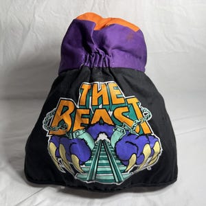 May include: Black drawstring bag with a colorful graphic of a monster claw and the words "THE BEAST" in orange and teal. The top of the bag is purple and orange.