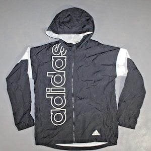 May include: Black and white Adidas windbreaker jacket with a zipper closure and a hood. The jacket has the Adidas logo on the left chest and the word "Adidas" printed vertically down the front.