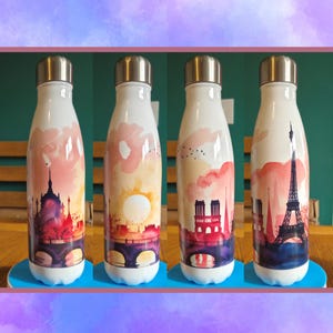 May include: A white metal water bottle featuring a wrap-around watercolor illustration of the Paris skyline. The design includes the Eiffel Tower, Notre-Dame Cathedral, and a bridge over the Seine, set against a sunset sky in shades of pink and orange.