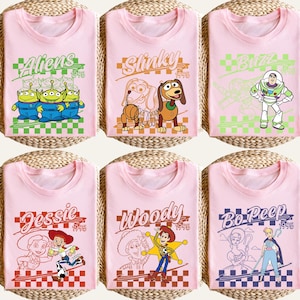 May include: Six pink t-shirts featuring characters from the animated film Toy Story. Each shirt has a different character design, including Aliens, Slinky, Buzz, Jessie, Woody, and Bo Peep, with the year 1995 displayed.