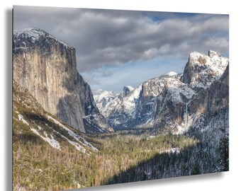 Könnte beinhalten: Landschaftsfotografie eines Bergtals im Winter. Das Bild zeigt schneebedeckte Berge, einen Wald und einen bewölkten Himmel. Die Beleuchtung erzeugt Schatten und Glanzlichter auf den Bergen und Bäumen.