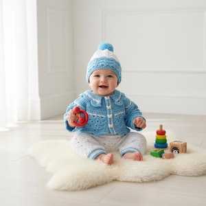 May include: A baby wearing a blue and white crochet hat, jacket, and pants set. The jacket has a Peter Pan collar and button closure. The baby is holding a red rattle and sitting on a white fluffy rug, with colorful wooden toys nearby.