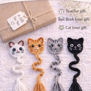 May include: Handmade cat-shaped bookmarks in white, orange, gray, and black. Each bookmark features a crocheted cat head with a long, twisted body and a tassel. The image includes a gift box and text that reads "A Gift For You."