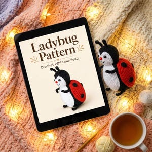 May include: A tablet displaying a Ladybug Pattern Crochet PDF Download with an illustration of a crocheted ladybug, alongside a physical crocheted ladybug toy featuring a black head, white body, and red wings with black spots.