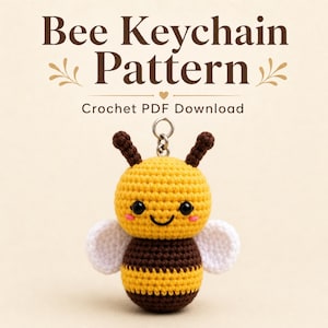 May include: A crochet bee keychain with a yellow and brown striped body, white wings, black eyes, and pink cheeks. The text above reads Bee Keychain Pattern Crochet PDF Download. The bee has two brown antennae and a silver metal keyring attachment.