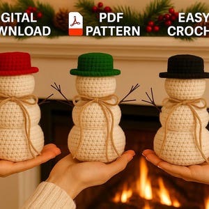 May include: Three crocheted snowmen with red, green, and black hats, each with twig arms and a twine scarf. The snowmen are held in hands. Text at the top reads "DIGITAL DOWNLOAD", "PDF PATTERN", and "EASY CROCHET".