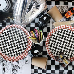 Op de afbeelding: Een feesttafel met een zwart-wit geblokt thema. Inclusief geblokte borden, kleurpotloden, speelgoed monstertrucks en een zilveren cijferballon. De tafel is gedekt voor een raceauto- of monstertruck-themafeest.