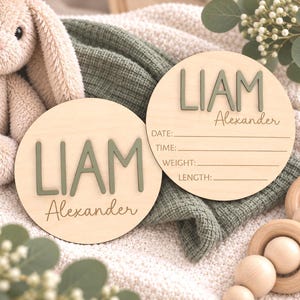 Puede incluir: Dos placas circulares de madera clara con el nombre LIAM en letras verdes salvia en relieve y Alexander en cursiva. Una placa incluye l&iacute;neas impresas para Fecha, Hora, Peso y Longitud para registrar los datos de nacimiento de un beb&eacute;.