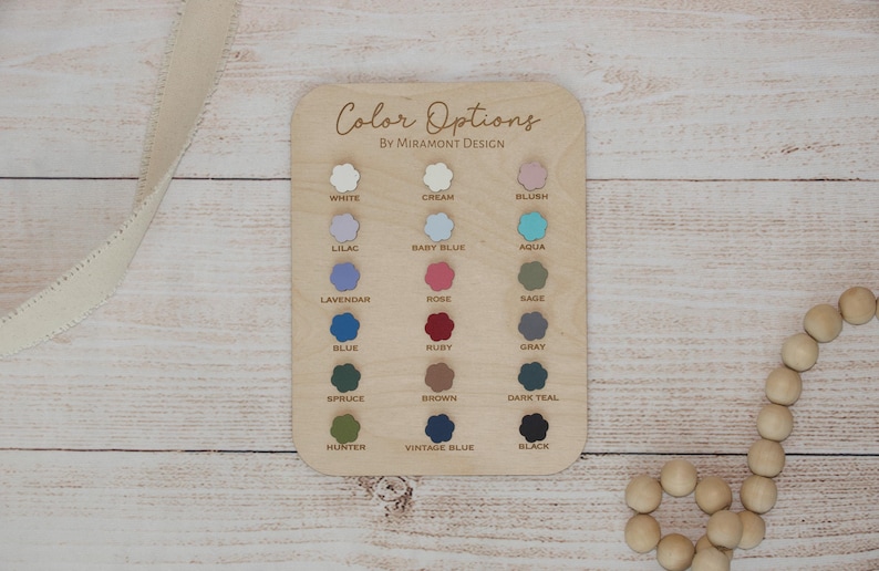 May include: A wooden colour chart with the text "Color Options by Miramont Design" and a selection of colour swatches. Colours include white, cream, blush, lilac, baby blue, aqua, lavender, rose, sage, blue, ruby, grey, spruce, brown, dark teal, hunter, vintage blue, and black.