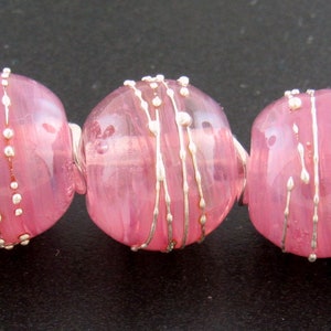 May include: Six pink glass beads with silver accents. The beads are round and have a swirl pattern. They are strung on a silver wire.