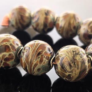 Könnte beinhalten: Eine Kette aus braunen, weißen und goldenen Glasperlen mit Marmormuster. Die Perlen sind rund und haben eine glänzende Oberfläche.