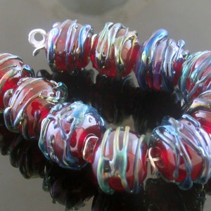 May include: A red glass bead bracelet with iridescent blue and green accents. The beads are round and have a textured surface. The bracelet is made of multiple beads strung together with a silver clasp.
