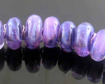 May include: A strand of artisan glass beads in shades of purple and blue. Each bead is cylindrical with a marbled effect, strung together with silver-colored metal loops. The beads are approximately 0.5 inches in length.