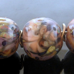 May include: A strand of five colorful glass beads with a silver clasp. The beads are round and have a marbled pattern with shades of brown, pink, and white.