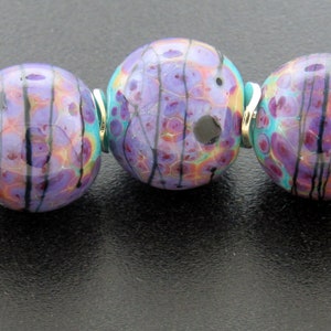 May include: A strand of six purple, turquoise, and black glass beads with silver accents. The beads are round and have a marbled pattern.