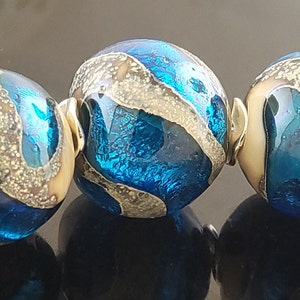 May include: A strand of six blue and gold glass beads with a silver connector. The beads have a swirling pattern of blue and gold.