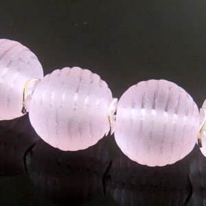 May include: A strand of pink glass beads with a silver clasp. The beads have a textured, ribbed surface.