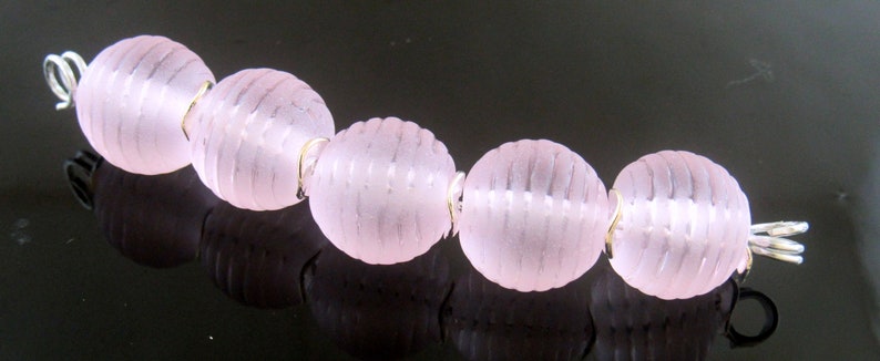 May include: A strand of pink glass beads with a silver clasp. The beads have a textured, ribbed surface.