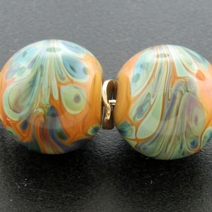 May include: Two glass beads with a swirling pattern of blue, green, and orange colors. The beads are connected by a gold metal connector.
