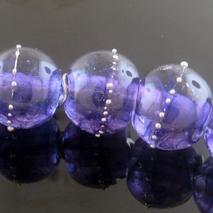 May include: A strand of purple glass beads with silver accents. The beads are round and have a slightly iridescent finish.