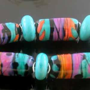 May include: A colorful bracelet made of turquoise and black glass beads with swirls of pink, orange, and teal. The beads are strung on a silver wire.