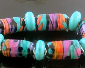 May include: A colorful bracelet made of turquoise and black glass beads with swirls of pink, orange, and teal. The beads are strung on a silver wire.