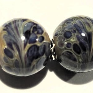 May include: Two round glass beads with a swirling pattern of beige, gray, and purple. The beads are connected by a silver metal loop.