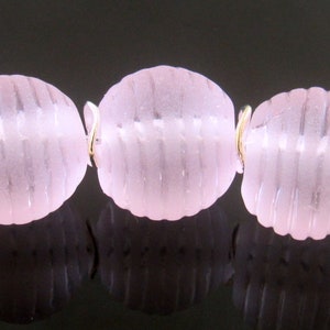 May include: A strand of six pink glass beads with a silver wire connecting them. The beads have a textured, ribbed surface.