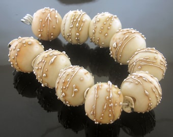 May include: A white beaded necklace with silver accents. The beads are round and have a textured surface. The necklace is strung on a silver wire.