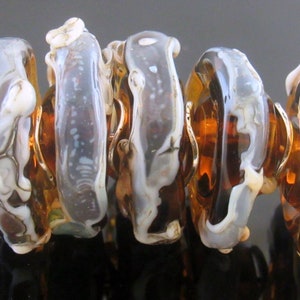 May include: A set of six glass beads with a swirling pattern of white and brown. The beads are strung together with gold wire and have a silver clasp.