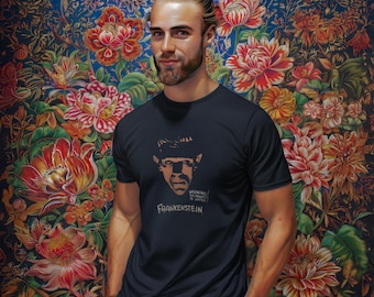 May include: Navy blue t-shirt featuring a graphic of Frankenstein's monster with the text "WARNING: MONSTER IS LOOSE!" and "FRANKENSTEIN" in a vintage style. The shirt is worn in front of a floral background.