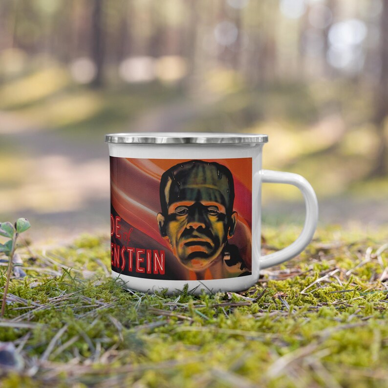 May include: White enamel mug featuring a vintage movie poster design of Frankenstein's monster. The mug has a silver rim and handle, with the monster's face and the word "Frankenstein" in red text.