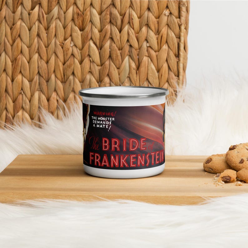 May include: White enamel mug with a silver rim featuring a design from the movie "The Bride of Frankenstein." The mug has the text "WARNING! THE MONSTER DEMANDS A MATE!" and "The Bride of Frankenstein" in red and white.