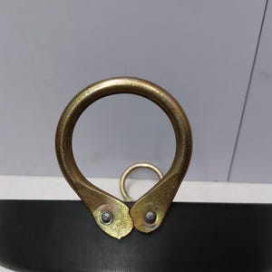 Peut inclure: Gros plan sur une marmite en m&eacute;tal noir avec une grande poign&eacute;e dor&eacute;e. La poign&eacute;e est un anneau arrondi fix&eacute; &agrave; la marmite avec deux supports dor&eacute;s. Un anneau dor&eacute; plus petit est visible en arri&egrave;re-plan.