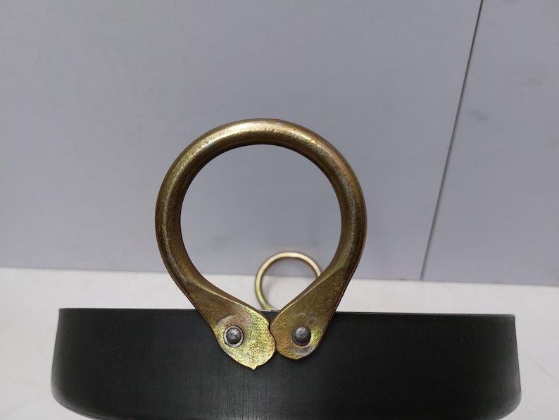 Peut inclure: Gros plan sur une marmite en m&eacute;tal noir avec une grande poign&eacute;e dor&eacute;e. La poign&eacute;e est un anneau arrondi fix&eacute; &agrave; la marmite avec deux supports dor&eacute;s. Un anneau dor&eacute; plus petit est visible en arri&egrave;re-plan.