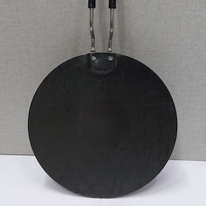 May include: A black, round griddle pan with a long handle. The handle is black with a silver metal support. The pan is made of a dark metal and is designed for cooking. The pan is approximately 10 inches in diameter.