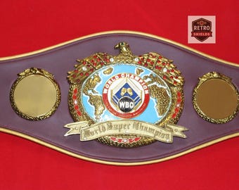 May include: A World Boxing Organization (WBO) Super Champion belt. The belt features a gold eagle emblem, a blue and white globe, and the words "World Super Champion." The belt is purple with gold accents.