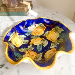May include: A ceramic bowl with a scalloped edge featuring a vibrant cobalt blue interior decorated with hand-painted yellow lemons and green leaves. The rim of the bowl is finished with a solid yellow border, contrasting against the deep blue.