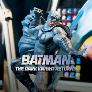 Puede incluir: Estatua detallada de Batman en una pose dinámica, con una expresión severa. La figura es predominantemente gris y negra, con el texto "BATMAN THE DARK KNIGHT RETURNS" en la base. La estatua captura el físico musculoso y la icónica capucha del personaje.