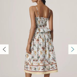 May include: A two-piece dress with a white background and a colourful floral pattern. The top has thin straps and a ruffled hem. The skirt is knee-length with a yellow border. The model is wearing brown heels.